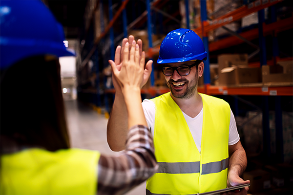 Two workers in safety gear high-five in a warehouse, possibly celebrating a successful workers' comp case.