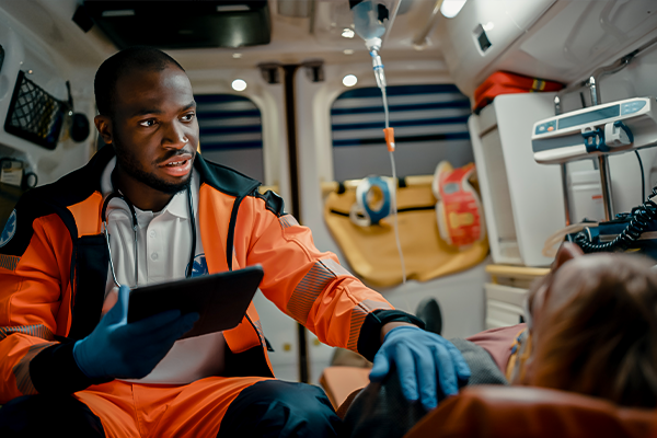 A paramedic in an orange uniform is attending to a patient in an ambulance, representing the medical care aspect of the workers' compensation process.