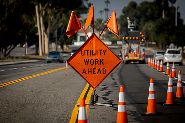 An orange 'UTILITY WORK AHEAD' sign and traffic cones set up on a street, indicating a work zone that may involve considerations for worker safety and compensation.