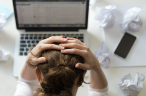 woman grabbing her head in front of her laptop